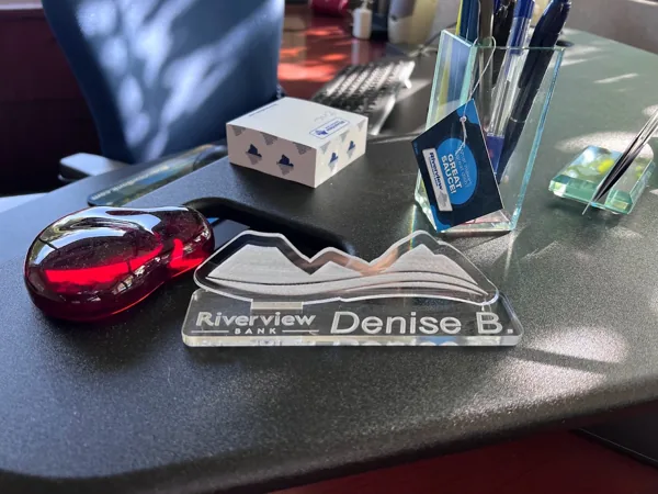 Clear acrylic Riverview Bank mountain-logo desk nameplate on a desk.